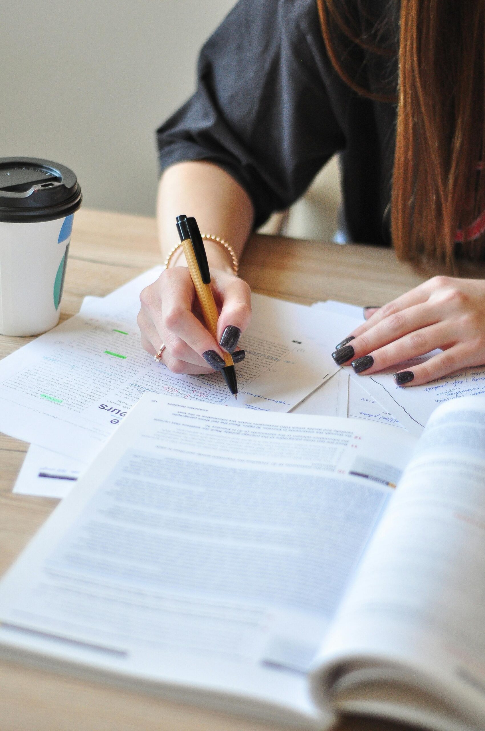 A young woman studying with a pen and coffee cup, focusing on her notes.