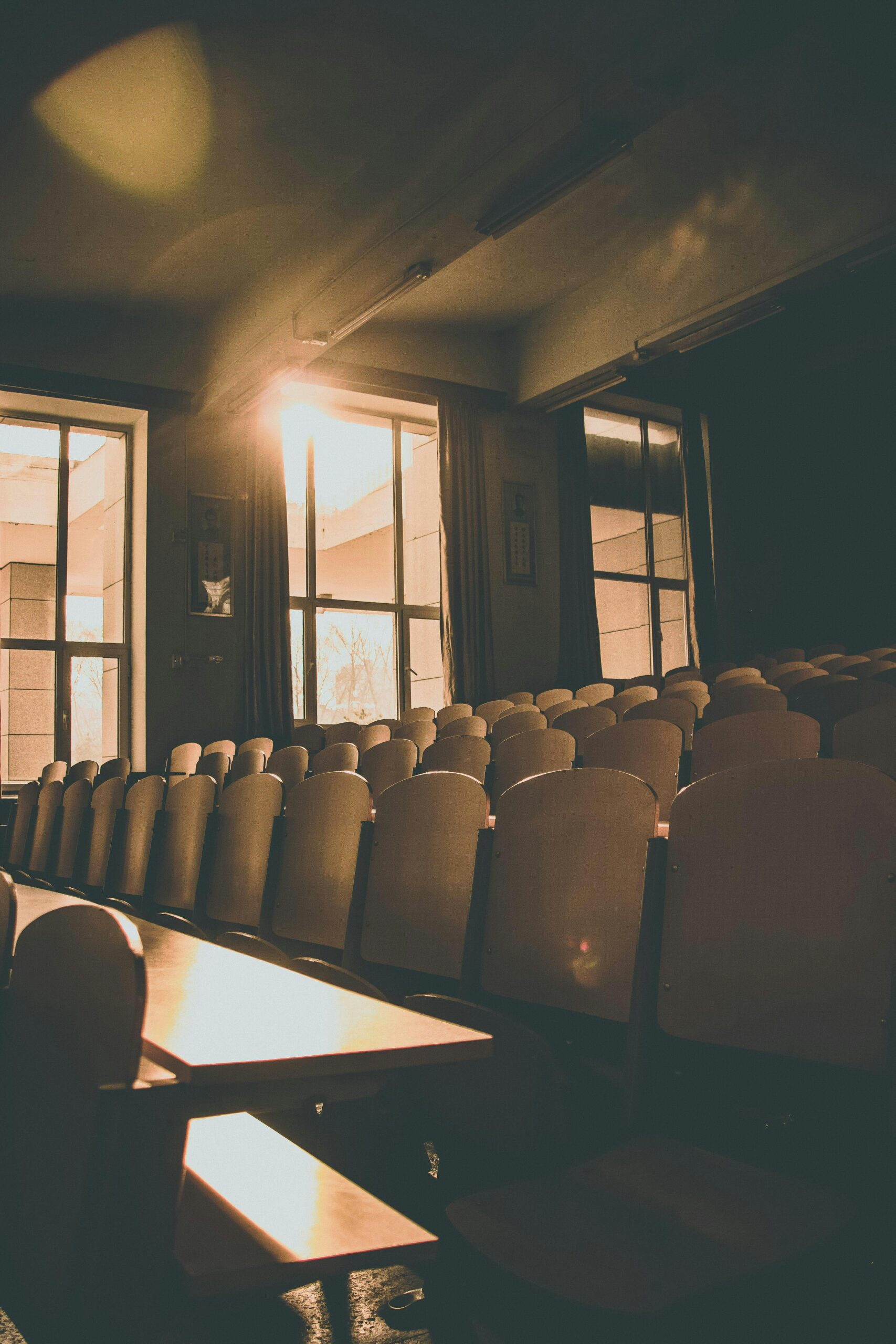 Sunlit auditorium with rows of empty wooden chairs and warm tones, ideal for indoor architecture themes.